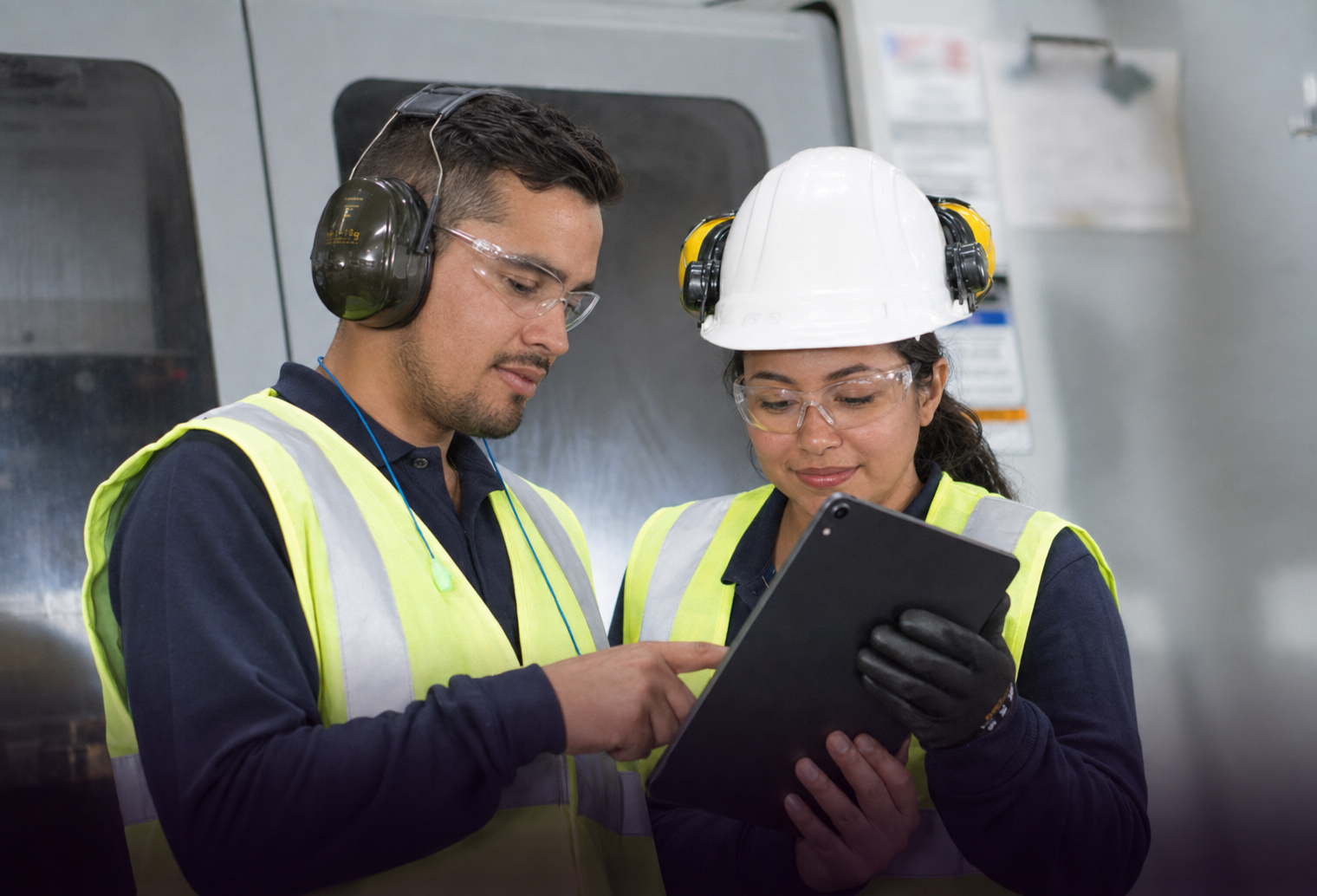 Texticom-ingeniería-en-plásticos hombre adulto y señorita joven con casco blanco en ambiente laboral usando chalecos reflectivos y con tablet en mano